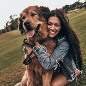 A woman hugs her dog while sitting on the grass A middle aged woman sits on the grass with her dog outside showing it affection with a big hug.